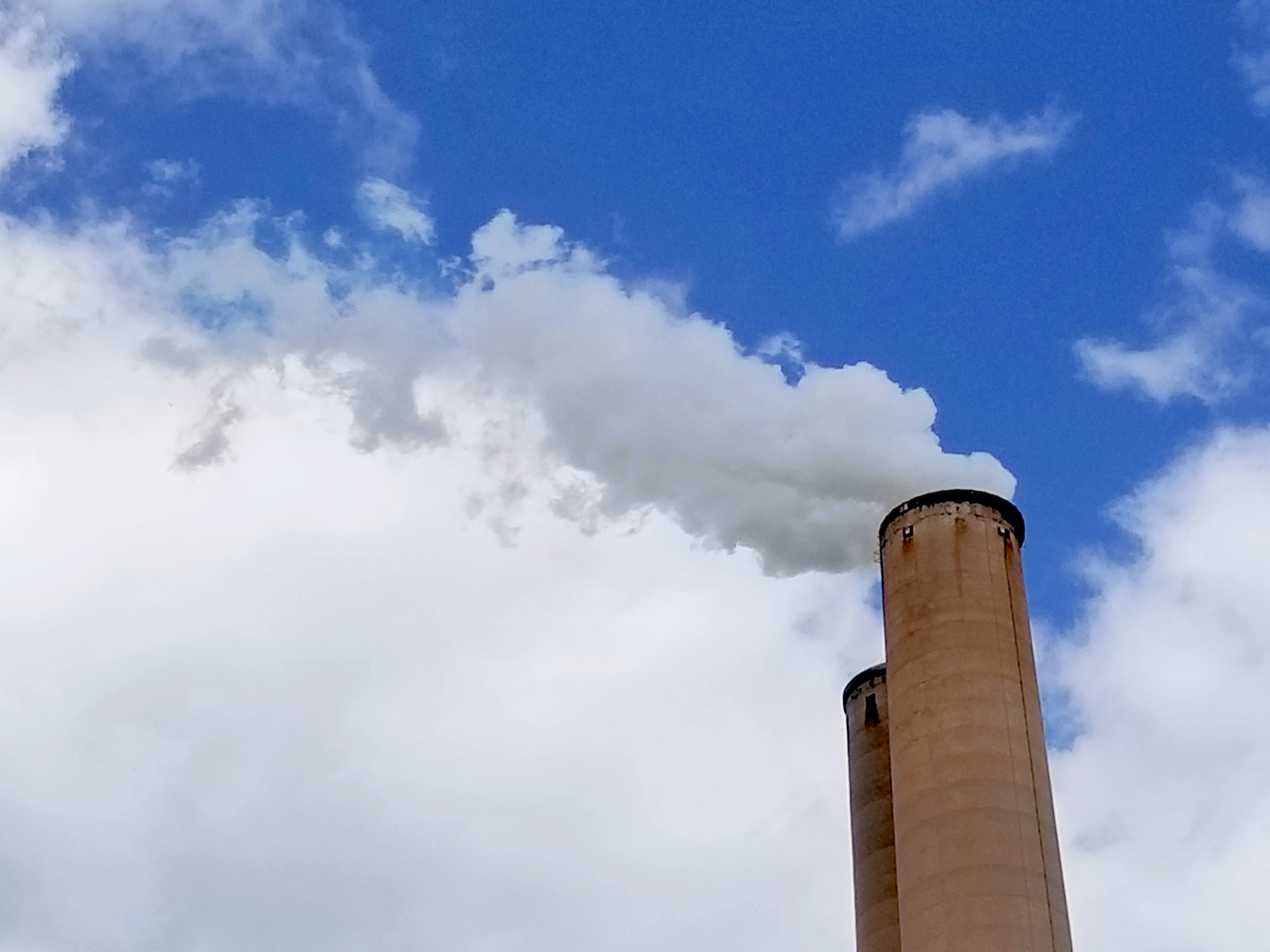 Smokestacks with billowing grey smoke coming out of them are seen in stark contrast to a bright blue
