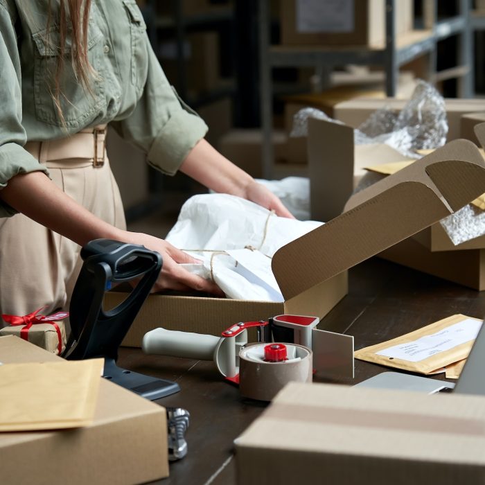 Female online store business owner packing ecommerce shipping box.